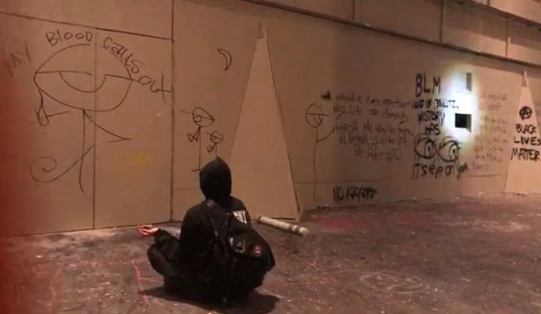 Protester meditating in front of graffiti